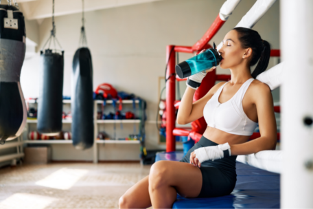 Female Athlete Sitting on the Edge of a Boxing Ring Drinking Water for Hydration