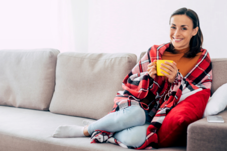 Woman sitting on couch wrapped in red blanket holding a yellow mug with menstrual abnormalities