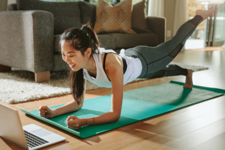 Woman exercising on green yoga mat looking at laptop in front of her work life sport balance