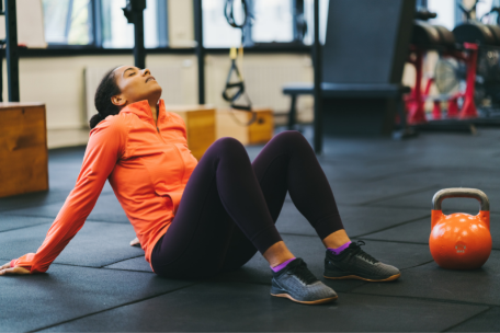 Woman in activewear sitting on the ground of a gym next to kettlebells fatigue