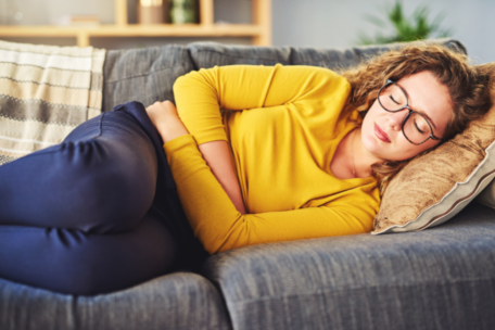 Woman in yellow sweater lying on couch holding her stomach in pain from endometriosis