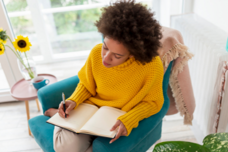 Woman in yellow sweater sitting on chair writing in a book stress management